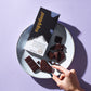 Dark chocolate bar on cream plate with hand holding chocolate on purple background